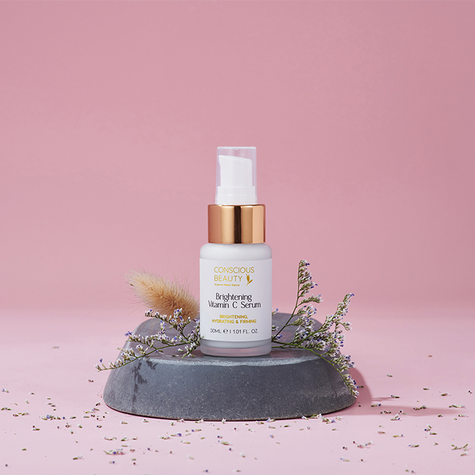 Brightening Vitamin C Serum 30ml on a stone with flowers, for sensitive, eczema-prone, and autoimmune skin, against a pink background.