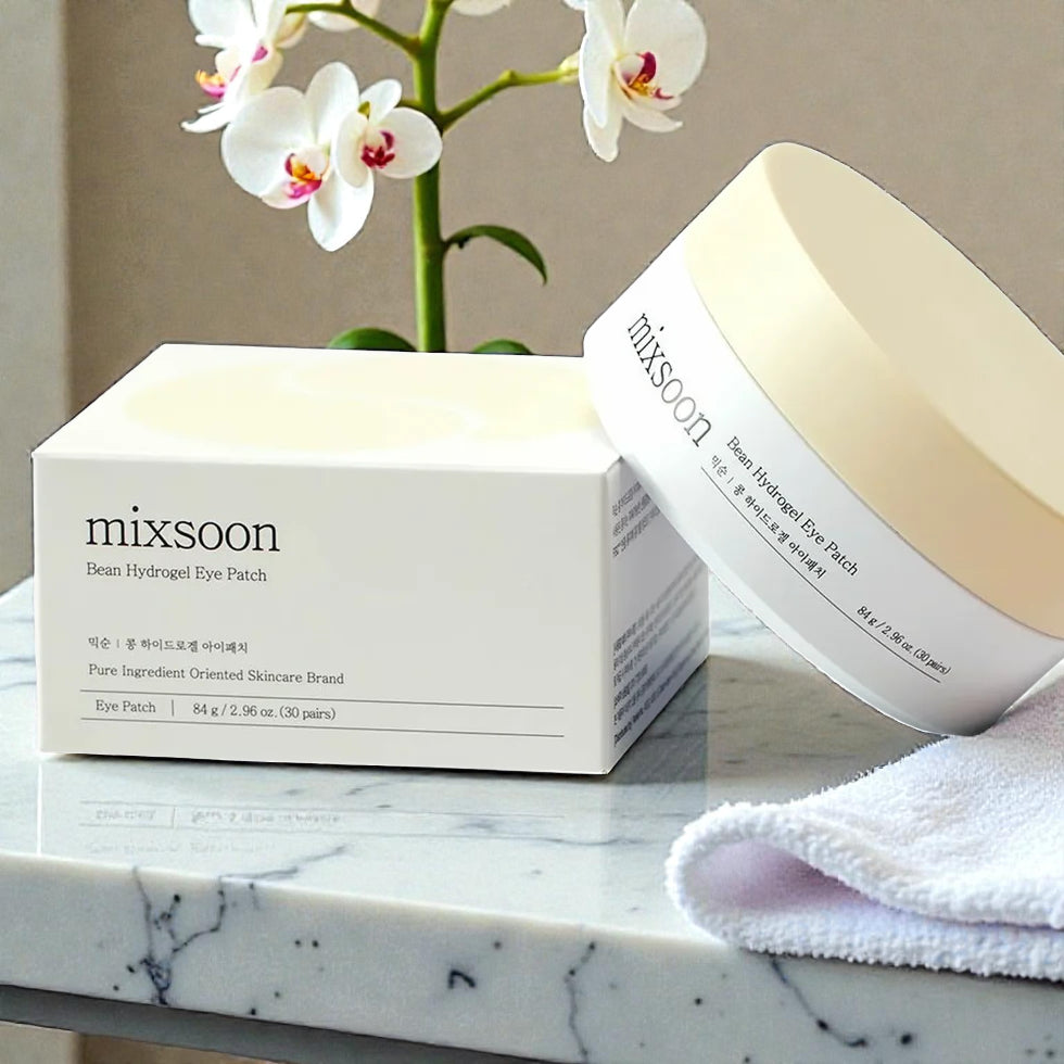 Mixsoon Bean Hydrogel Eye Patch box and jar displayed on a marble surface with towel and orchid