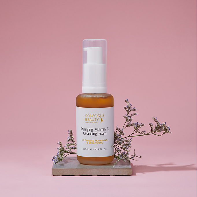 Purifying Vitamin C Cleansing Foam 100ml placed on a stone with floral accents against a pink background, ideal for sensitive skin.