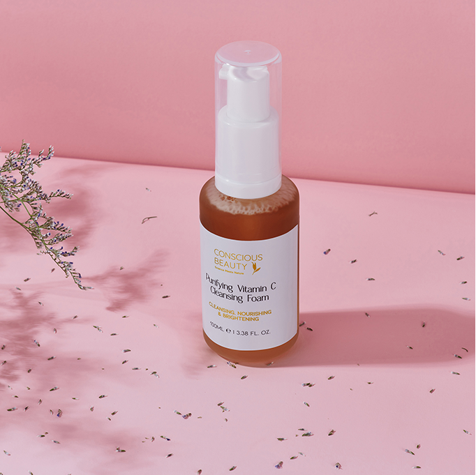 Purifying Vitamin C Cleansing Foam 100ml on a pink surface with soft shadows and flowers, formulated for eczema-prone and autoimmune skin.