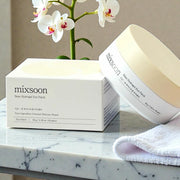 Mixsoon Bean Hydrogel Eye Patch box and jar displayed on a marble surface with towel and orchid