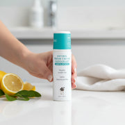 Hand holding MooGoo Natural Fresh Cream Deodorant with lemon myrtle in a clean bathroom setting