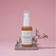 Purifying Vitamin C Cleansing Foam 100ml placed on a stone with floral accents against a pink background, ideal for sensitive skin.