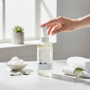 Hand pressing pump of Round Lab 1025 Dokdo Cleansing Oil 200ml on marble counter with cotton pads